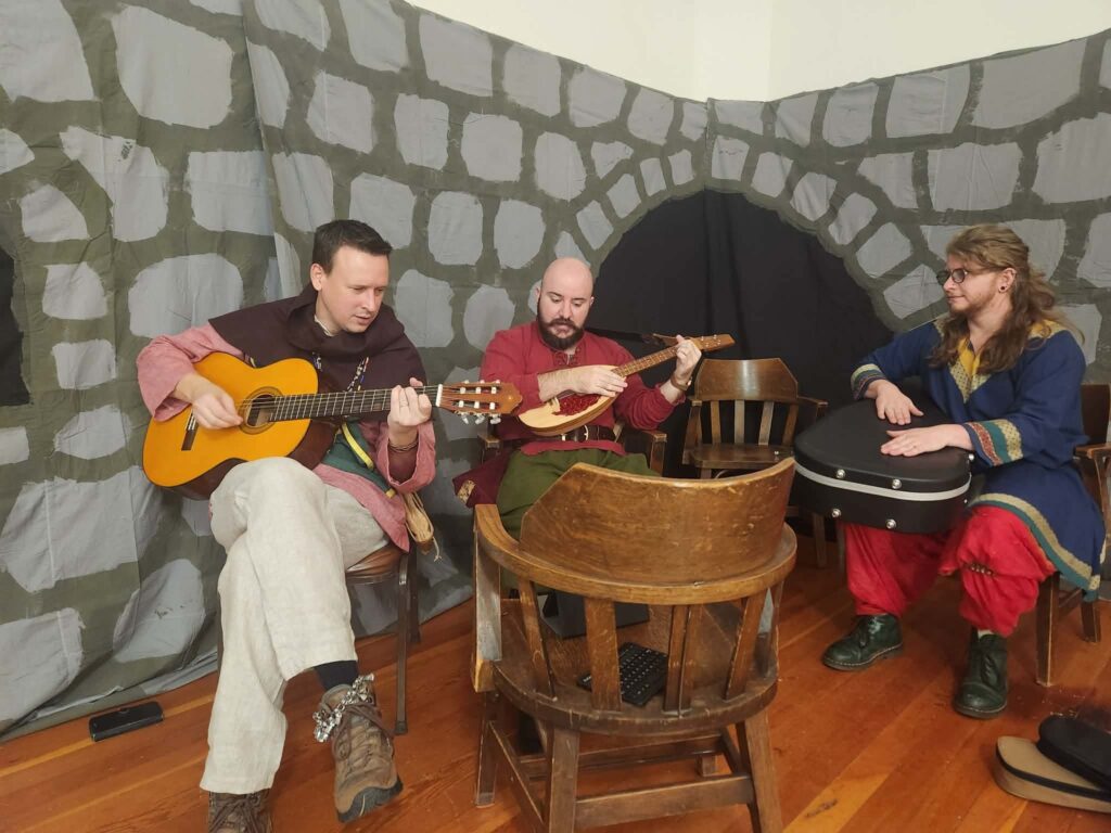 Three musicians sit in a corner playing.